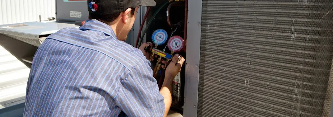 HVAC technician servicing a condenser unit in Millis