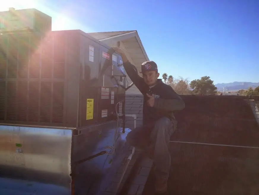 HVAC technician performing Air Duct Cleaning on a rooftop unit in Millis